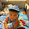 baby, child, infant, blue_cap, bed, bedroom, blanket, bedspread, crawling, sitting, portrait, face, eyes, smiling, clothing, toy, stuffed_animal, indoor, home, colorful