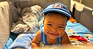 Jaci is registered to the contest to win money with this photo: child, toddler, baby, smiling, portrait, face, blue_cap, tank_top, bed, bedroom, blankets, bedding, indoors, cozy, warm_lighting, happy, lying_down, looking_at_camera, home, photography