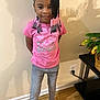 Kehlani is registered to the contest to win money with this photo: child, girl, indoor, standing, pink_tshirt, barbie, braided_hair, beads, smile, jeans, pink_slippers, plant, table, wooden_floor, wall, power_outlet, shadow, casual_clothing, cute, portrait