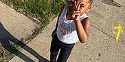 Kehlani is registered to the contest to win money with this photo: child, girl, peace_sign, braided_hair, beads, white_tank_top, black_pants, pink_slides, sidewalk, grass, sunny, shadow, outdoor, casual_clothing, smiling, standing, playful, happy, person, summer