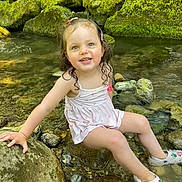 Romy a rejoint le concours — aidez-le/la à gagner de superbes lots ! child, toddler, smiling, water, rocks, stream, moss, nature, outdoor, wet_hair, white_dress, crocs, playful, summer, happy, cute, sitting, sunlight, green, feet_in_water