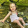 child, toddler, smiling, water, rocks, stream, moss, nature, outdoor, wet_hair, white_dress, crocs, playful, summer, happy, cute, sitting, sunlight, green, feet_in_water