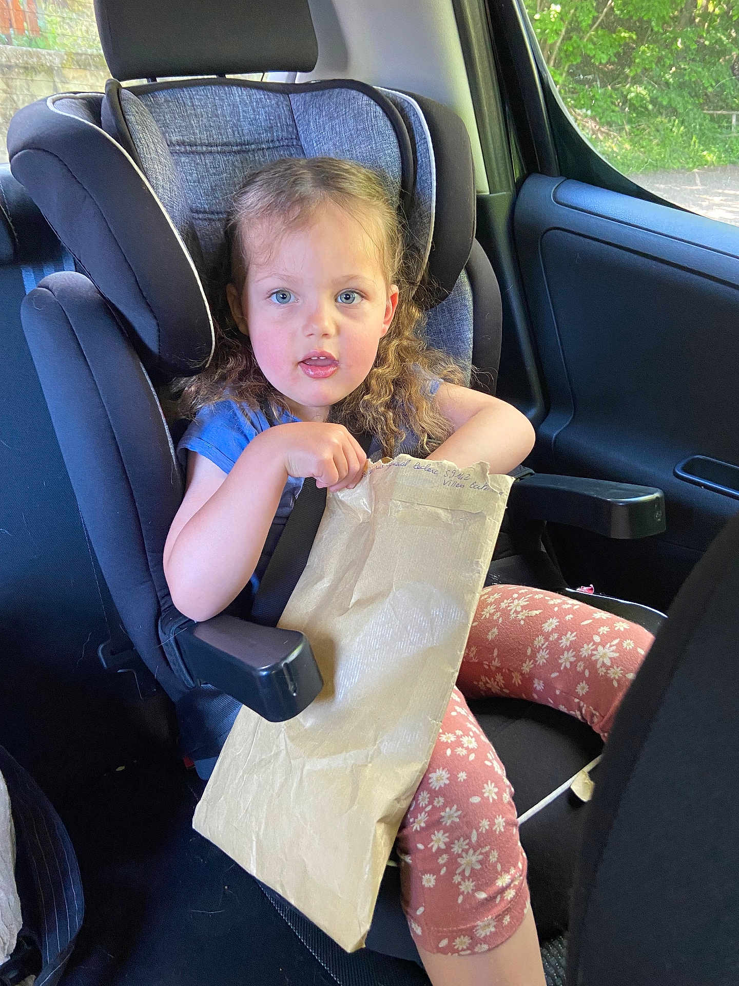 Romy a rejoint le concours — aidez-le/la à gagner de superbes lots ! child, car_seat, blue_shirt, curly_hair, paper_bag, floral_leggings, car_interior, seatbelt, window, daylight, young_girl, sitting, holding, curious, casual_clothing, safety, transportation, cute, portrait, indoors