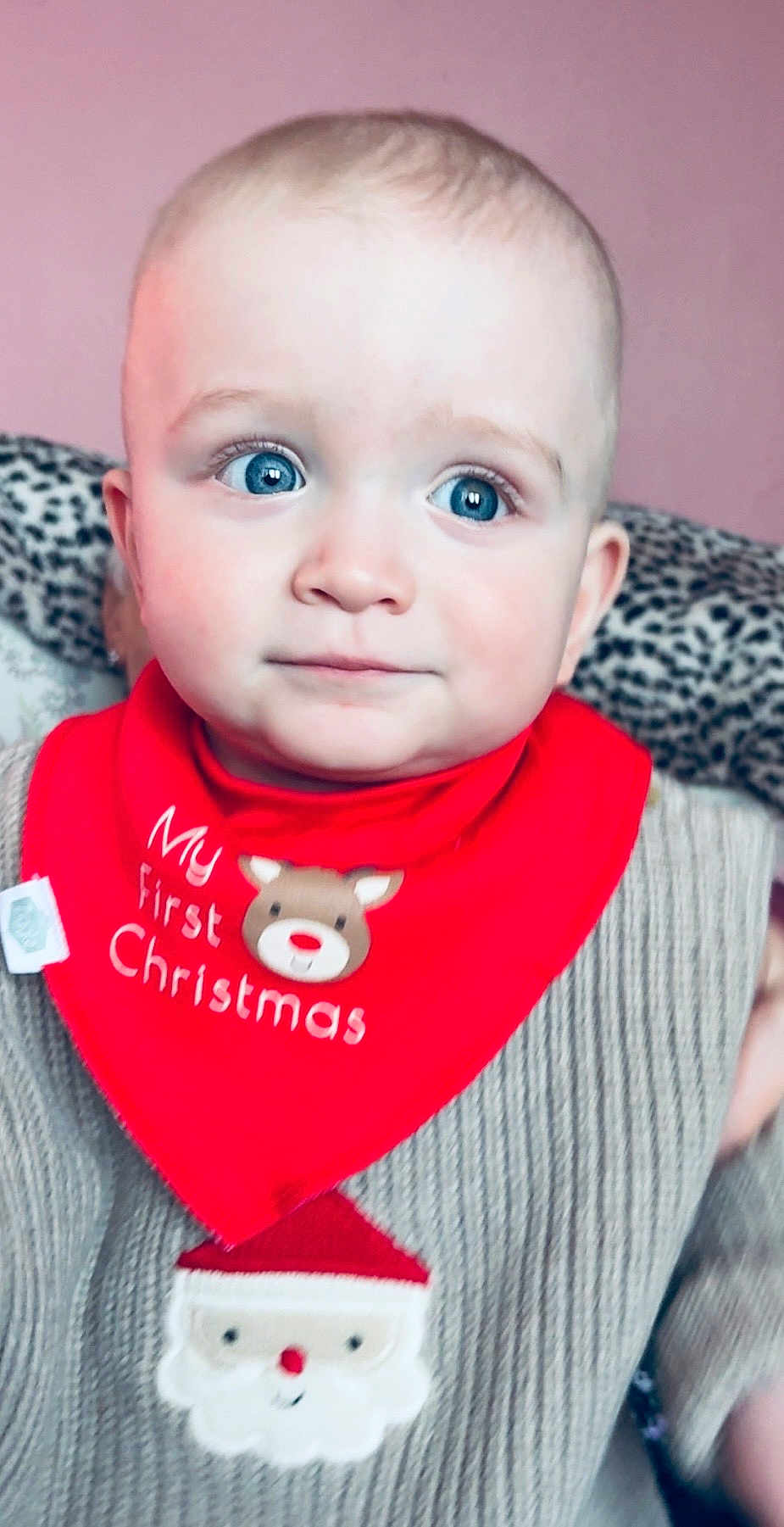 Jacob is registered to the contest to win money with this photo: baby, child, blue_eyes, red_bib, christmas, santa, sweater, knitwear, face, portrait, indoor, cute, holiday, festive, smile, young_child, person, closeup, pink_background, leopard_print