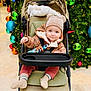 Jacob is registered to the contest to win money with this photo: baby, child, stroller, winter_clothing, hat, bear_ears, christmas_tree, ornaments, holiday, festive, lights, smiling, indoors, floor, blanket, happy, cute, person, seated, toddler