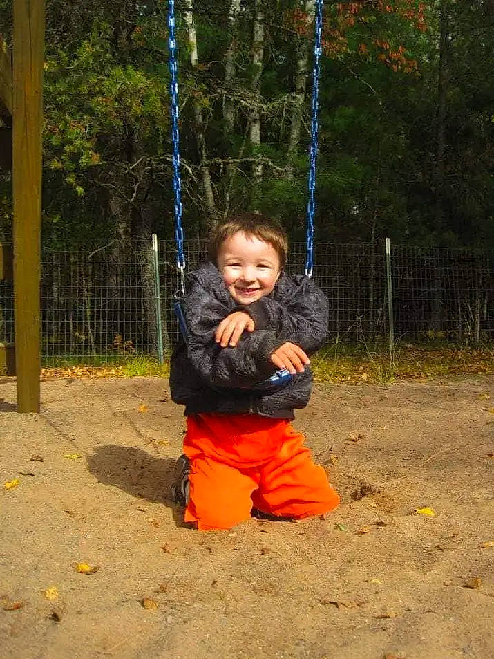 Valentino is registered to the contest to win money with this photo: baby, baby_toddler_clothing, city, electric_blue, fun, grass, happy, jacket, joy, leisure, outdoor_play_equipment, people_in_nature, person, plant, playground, recreation, sleeve, smile, soil, swing