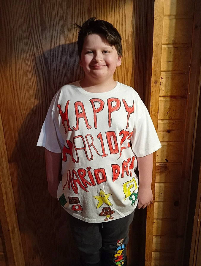 Rocco is registered to the contest to win money with this photo: active_shirt, bangs, face, flesh, font, fun, hair, happy, hardwood, jaw, joy, neck, pattern, person, sleeve, smile, sportswear, t_shirt, toddler, top