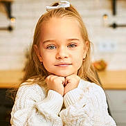 Lucia joined the competition — help win amazing prizes! child, girl, portrait, face, white_sweater, hair_bow, blonde_hair, indoors, kitchen, warm_lighting, resting_chin, cute, young, smiling_slightly, casual_clothing, earrings, cozy, background_blur, home, person