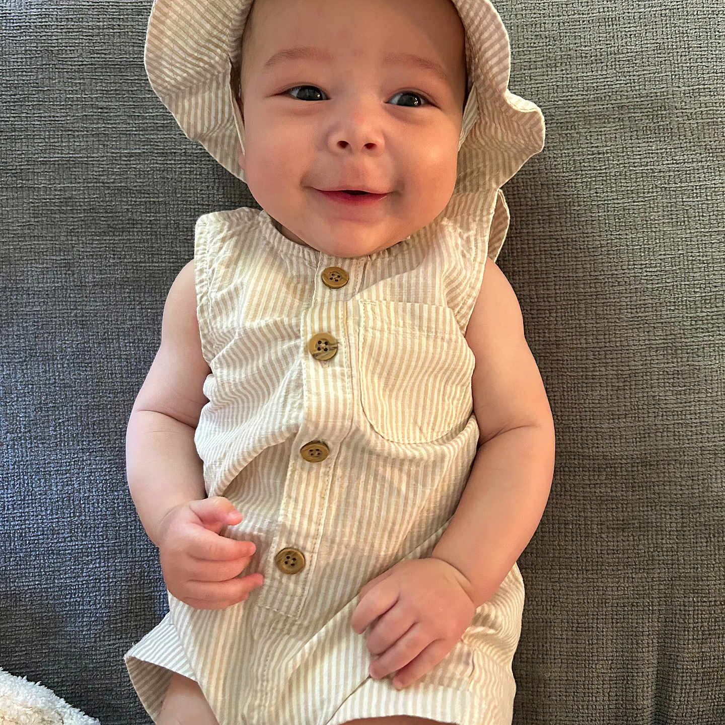 Ldarian is registered to the contest to win money with this photo: baby, buttoned, child, clothing, cute, fabric, face, hand, happy, hat, indoors, infant, legs, lying, person, skin, sleeveless, smiling, striped, texture