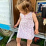 barefoot, casual, child, curly_hair, daylight, doorway, dress, floral_pattern, grass, hair_tie, looking_down, outdoor, person, playful, rug, standing, summer, toddler, trailer, young_child