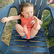 Alycia participe au concours pour gagner de l'argent avec cette photo : black_chair, blue_eyes, blue_shorts, casual_clothing, child, curious_expression, curly_hair, daylight, feet_up, grass, nature, orange_tank_top, outdoor, person, plastic_chair, playful, sitting, summer, toddler, young_child