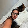 Boomie is registered to the contest to win money with this photo: woman, glasses, cat, selfie, couch, snuggling, affection, cozy, indoor, pet, fur, white_couch, brown_hair, casual, relaxing, smiling, face, closeup, comfort, home