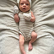 Willow is registered to the contest to win money with this photo: baby, newborn, infant, blanket, headband, mittens, knitted, romper, lying_down, soft_texture, cute, small_feet, small_hands, portrait, indoors, cozy, sleepwear, neutral_colors, closeup, child