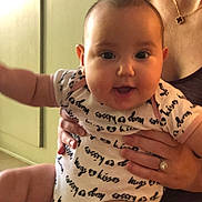 Rebecca joined the competition — help win amazing prizes! baby, infant, child, person, smile, happy, onesie, clothing, hand, adult, jewelry, necklace, ring, indoor, wall, floor, furniture, holding, closeup, portrait