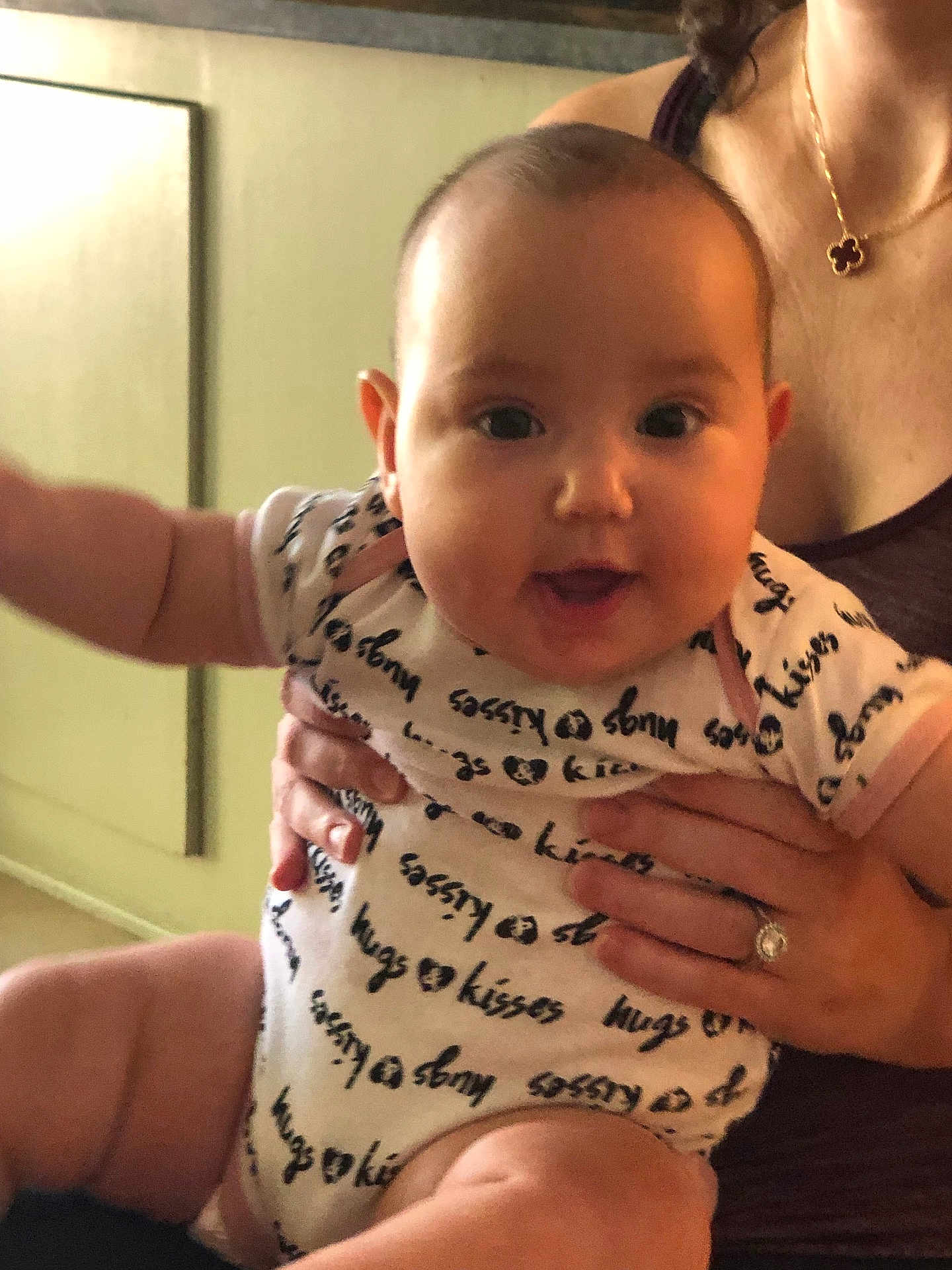 Rebecca joined the competition — help win amazing prizes! baby, infant, child, person, smile, happy, onesie, clothing, hand, adult, jewelry, necklace, ring, indoor, wall, floor, furniture, holding, closeup, portrait