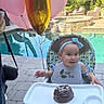 baby, high_chair, cake, balloons, pool, outdoor, celebration, headband, bib, smiling, child, chocolate_cake, party, sunlight, footwear, pavement, greenery, wicker_chair, water, fun