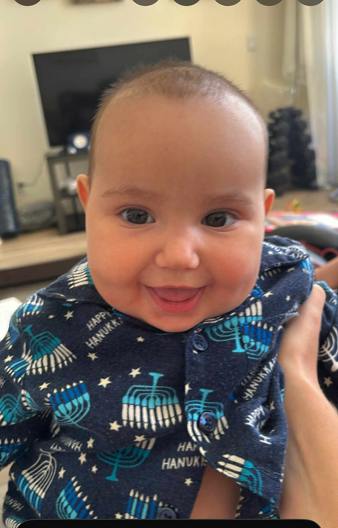Rebecca is registered to the contest to win money with this photo: baby, child, smiling, indoor, face, person, clothing, pattern, hanukkah, menorah, celebration, happy, cute, portrait, hand, furniture, television, home, buttoned_shirt, infant