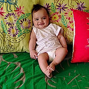 Kiana a rejoint le concours — aidez-le/la à gagner de superbes lots ! baby, child, smile, couch, pillow, embroidery, colorful, striped_clothing, diaper, indoor, happy, infant, person, sitting, green, red, fabric, cozy, cute, portrait