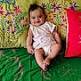 baby, child, smile, couch, pillow, embroidery, colorful, striped_clothing, diaper, indoor, happy, infant, person, sitting, green, red, fabric, cozy, cute, portrait