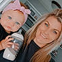 Aryanna joined the competition — help win amazing prizes! baby, woman, bottle, milk, headband, pink, blue_eyes, smile, long_hair, indoor, kitchen, person, holding, clothing, black_shirt, portrait, face, hand, child, family