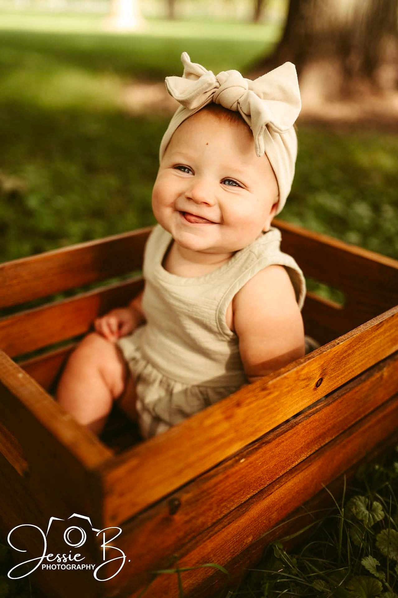 Aryanna is registered to the contest to win money with this photo: baby, child, smile, headband, bow, wooden_crate, outdoor, grass, greenery, portrait, cute, happy, toddler, infant, nature, sunlight, clothing, person, sitting, photography