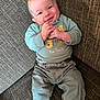 baby, infant, smiling, clothing, green_shirt, pants, socks, couch, fabric, texture, happy, portrait, indoor, person, child, cute, hands, face, seated, cozy