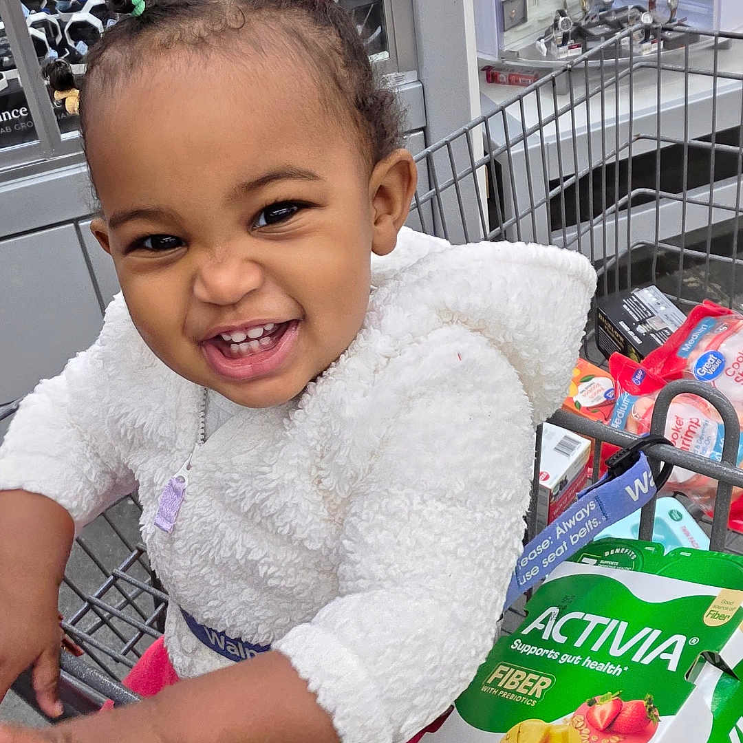 Reyna Melodie Alexis is registered to the contest to win money with this photo: activia, child, cute, fiber, food, grocery_store, hair_ties, happy, infant, person, pink_pants, playful, retail, shopping, shopping_cart, smile, store_aisle, toddler, white_jacket, yogurt