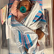 Keore is registered to the contest to win money with this photo: newborn, baby, pacifier, hospital_bassinet, blanket, swaddled, sleeping, headband, infant, hospital, baby_clothes, peaceful, cute, child, human, skin, foot, hand, indoor, healthcare