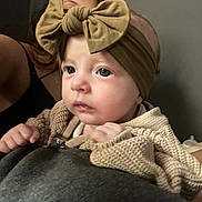 Shiloh joined the competition — help win amazing prizes! baby, child, headband, bow, knitted_sweater, close_up, face, portrait, indoor, person, cute, infant, young_child, clothing, skin, expression, looking, holding, soft_light, warm_tones