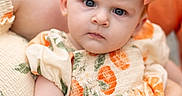 Marnie joined the competition — help win amazing prizes! baby, child, infant, dress, headband, bow, blue_eyes, serious_expression, holding, person, closeup, portrait, skin, arm, fabric, pattern, orange, peach, summer, outdoor