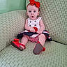 baby, child, girl, red_bow, red_shoes, white_dress, green_couch, textured_couch, surprised_expression, headband, sitting, indoor, cute, portrait, infant, clothing, face, person, footwear, furniture