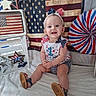 baby, child, smiling, sitting, patriotic, red_white_blue, headband, bows, american_flag, stars, stripes, celebration, holiday, clothing, footwear, crate, decor, indoor, portrait, happy