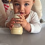 Léon a rejoint le concours — aidez-le/la à gagner de superbes lots ! baby, blue_eyes, bottle, child, closeup, cute, face, feeding, hand, high_chair, indoor, infant, milk, patterned_cushion, person, sitting, table, toddler, wall, white_clothing