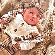 Aria a rejoint le concours — aidez-le/la à gagner de superbes lots ! baby, infant, plaid, bow, dress, fur_blanket, cozy, cute, child, portrait, soft_texture, warm, fashion, headband, newborn, person, closeup, indoors, comfortable, resting