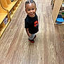 Ayden is registered to the contest to win money with this photo: toddler, child, smiling, standing, braided_hair, black_shirt, jeans, red_shoes, wooden_floor, classroom, cubbies, toys, indoor, happy, person, young_child, daycare, casual_clothing, play_area, education