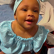 Aunesty is registered to the contest to win money with this photo: baby, child, smiling, headband, blue, dress, indoor, bed, blanket, person, cute, happy, portrait, infant, hand, sitting, skin, face, young, clothing