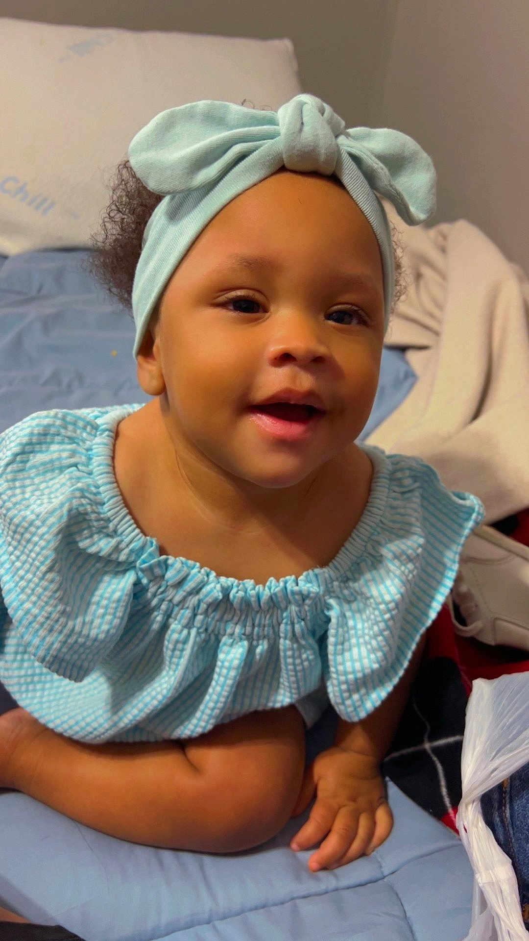 Aunesty is registered to the contest to win money with this photo: baby, child, smiling, headband, blue, dress, indoor, bed, blanket, person, cute, happy, portrait, infant, hand, sitting, skin, face, young, clothing