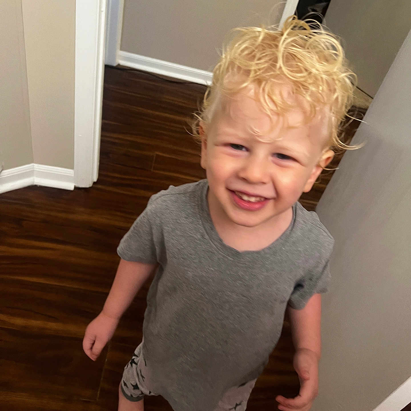 Avryall Apollo is registered to the contest to win money with this photo: barefoot, blonde, bright, casual_clothing, child, curly_hair, doorway, grey_tshirt, hallway, happy, home, indoor, person, portrait, smiling, standing, star_patterned_pants, toddler, wooden_floor, young_child