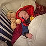 baby, bedding, blanket, child, cozy, crib, hooded_blanket, indoor, infant, nursery, pajamas, pillow, plush_toy, portrait, red_blanket, resting, sleeping, soft_light, stuffed_animal, white_rail