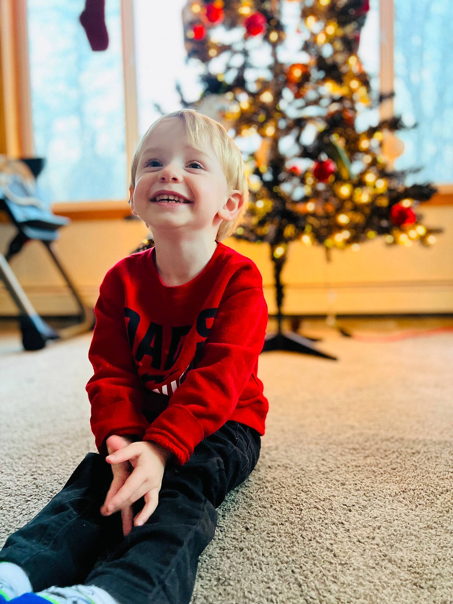 Brody is registered to the contest to win money with this photo: baby, baby_toddler_clothing, child, christmas_tree, event, facial_expression, flooring, fun, happy, jeans, joy, leisure, outerwear, person, plant, sleeve, smile, standing, t_shirt, toddler