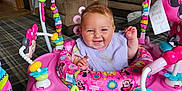 Bethany is registered to the contest to win money with this photo: baby, smiling, pink, jumper, toy, minnie_mouse, indoor, carpet, couch, living_room, child, happy, clothing, colorful, floor, person, playtime, furniture, infant, seat