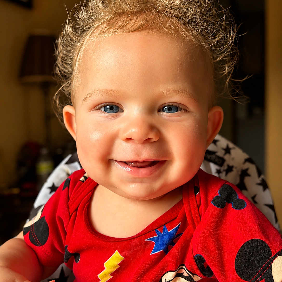 Jermaine is registered to the contest to win money with this photo: toddler, child, smiling, curly_hair, blue_eyes, red_shirt, mickey_mouse, high_chair, indoor, portrait, happy, cute, baby, person, clothing, face, expression, seated, warm_lighting, home