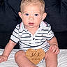 Jermaine is registered to the contest to win money with this photo: baby, infant, six_months, blue_eyes, curly_hair, striped_clothing, polo_shirt, wooden_sign, heart_shape, sitting, blanket, cushioned_background, cute, child, portrait, indoor, young_child, person, smiling, looking_at_camera