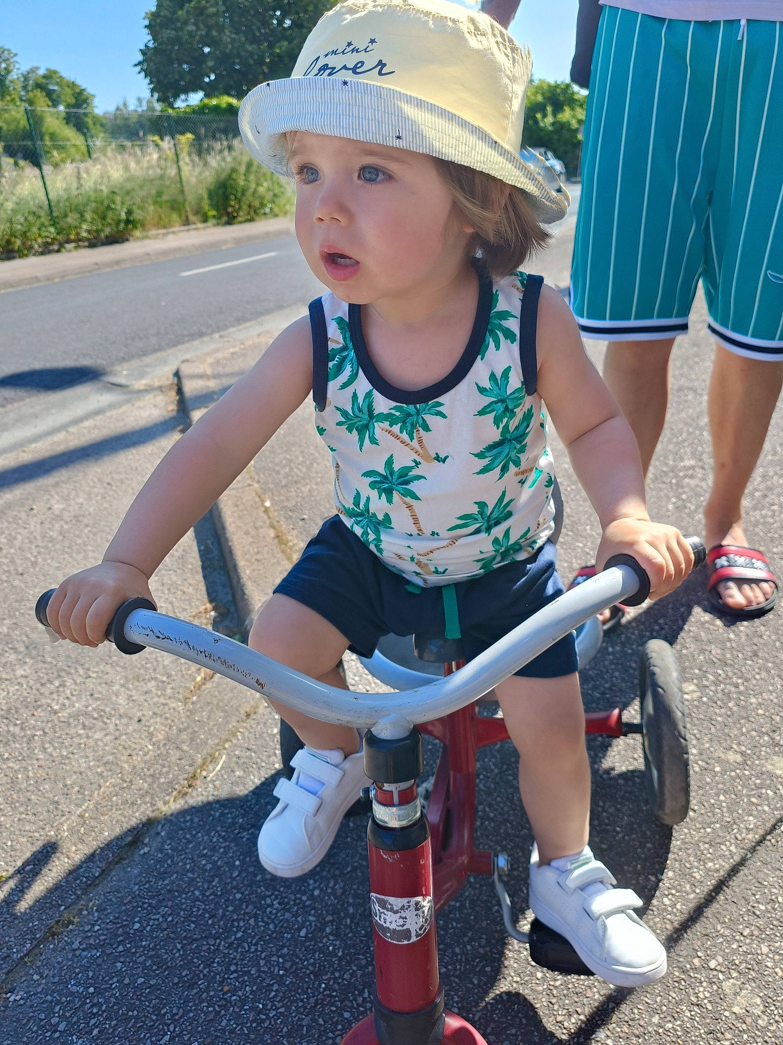 Juan a rejoint le concours — aidez-le/la à gagner de superbes lots ! asphalt, bicycle_accessory, bicycle_frame, bicycle_handlebar, bicycle_tire, bicycles_equipment_and_supplies, cap, child, fun, hat, headwear, leg, leisure, person, recreation, shorts, sneakers, sun_hat, tire, toddler