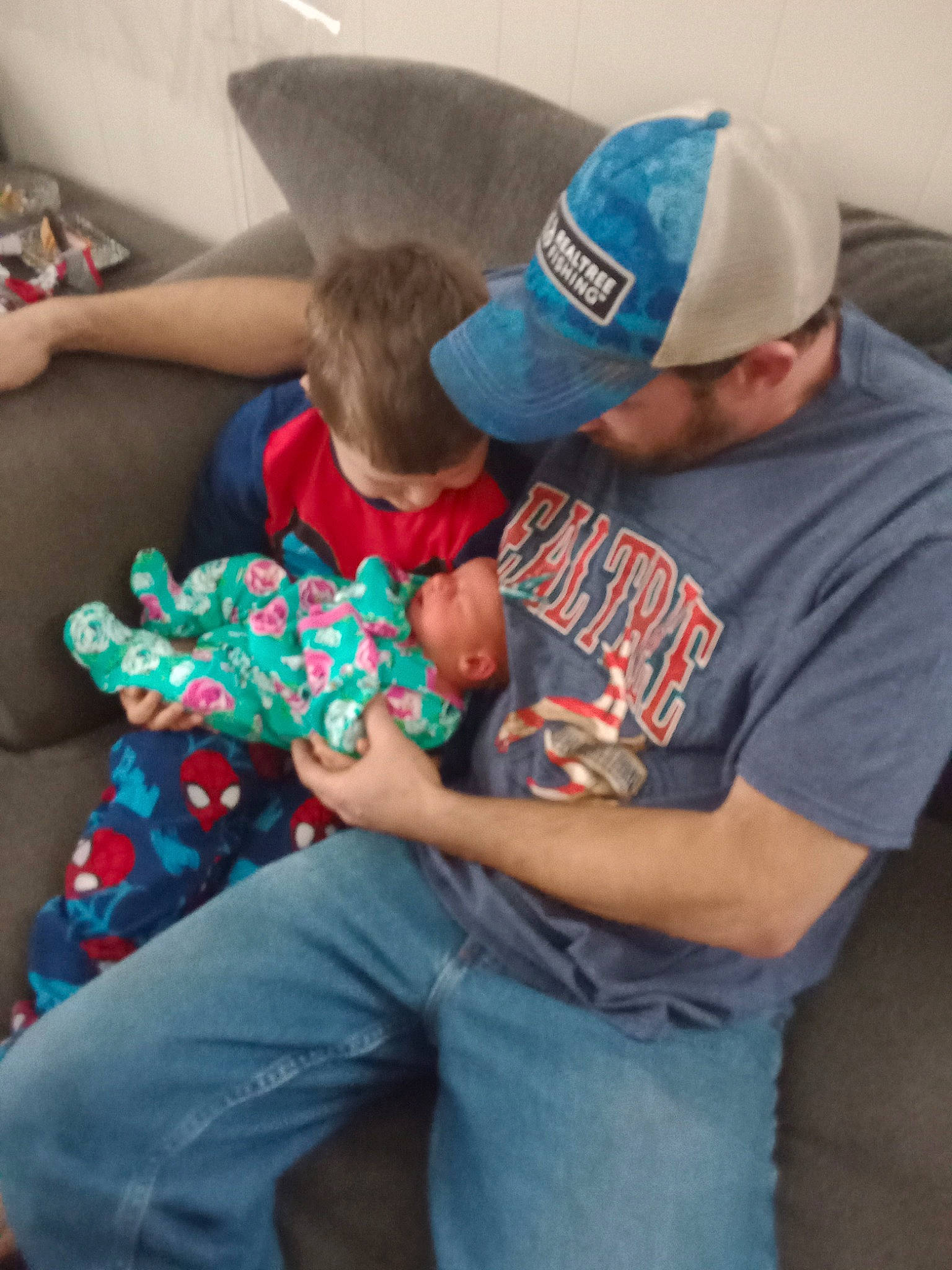 Clinton is registered to the contest to win money with this photo: arm, baby, baseball_cap, cap, child, comfort, couch, elbow, event, fun, hat, lap, leisure, person, play, shorts, sitting, t_shirt, thigh, toddler