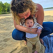 Nolann a rejoint le concours — aidez-le/la à gagner de superbes lots ! baby, woman, beach, sand, water, trees, sunlight, smile, happy, casual_clothing, jeans, sunglasses, blanket, nature, outdoor, family, affection, child, portrait, barefoot