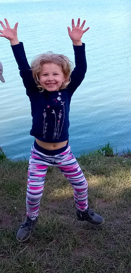 Hodéi participe au concours pour gagner de l'argent avec cette photo : active_pants, cool, electric_blue, footwear, gesture, grass, happy, human_body, joy, knee, lake, people_in_nature, person, plant, purple, sleeve, smile, t_shirt, thigh, toddler