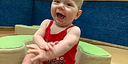 Charlie is registered to the contest to win money with this photo: baby, child, smiling, happy, clapping, indoor, play_area, tank_top, shorts, padded_seat, blue_wall, wooden_trim, young_child, cute, joyful, infant, person, sitting, casual_clothing, playroom