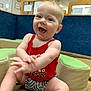 baby, child, smiling, happy, clapping, indoor, play_area, tank_top, shorts, padded_seat, blue_wall, wooden_trim, young_child, cute, joyful, infant, person, sitting, casual_clothing, playroom