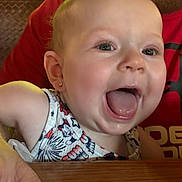 Charlie is registered to the contest to win money with this photo: baby, child, smiling, happy, face, person, infant, table, clothing, patterned, earring, adult, red_shirt, skin, cheerful, indoor, closeup, mouth_open, eyes, joy
